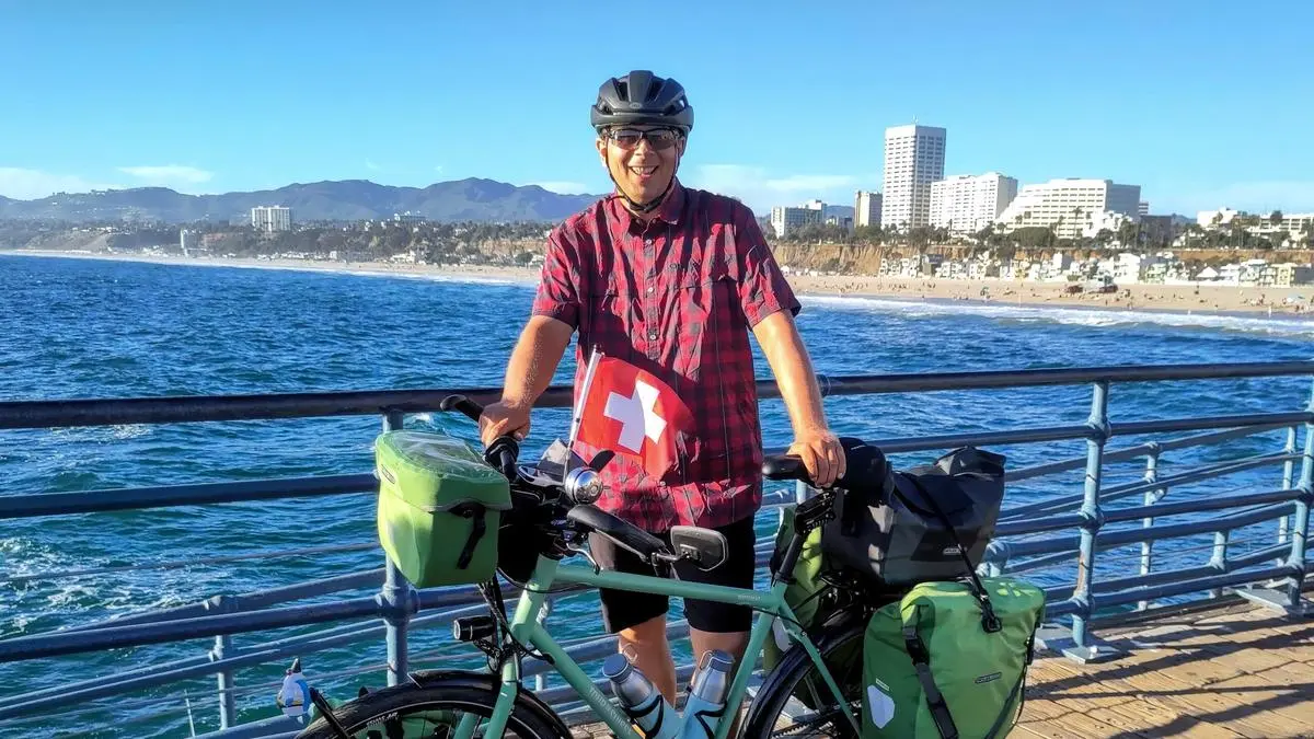 Der Artikel-Header von zentralplus mit einem Foto von mir und meinem Velo auf dem Santa Monica Pier im Vorderung mit dem Pazifik und der Skyline im Hintergrund